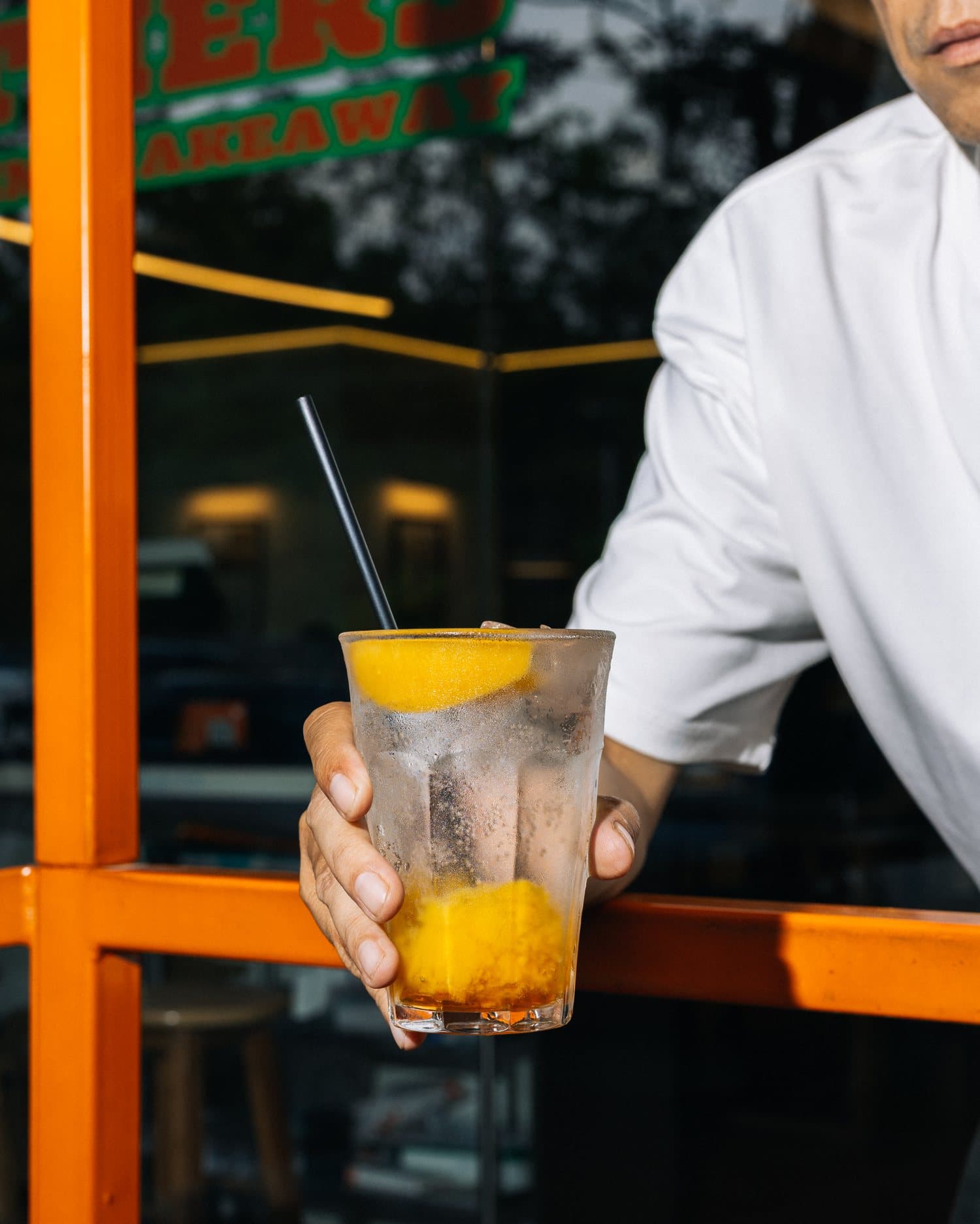 Barista holding an iced drink by the orange shopfront